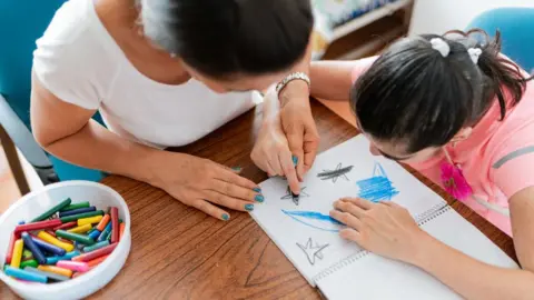 Getty Images Woman caring for child with learning disabilities, who is drawing