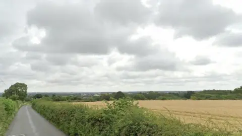 Google Rural road passing a field lined by hedges