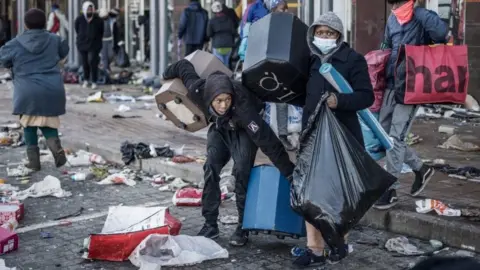AFP via Getty Images Looters take away few items left to grab in a vandalised mall in Vosloorus, on July 14, 2021