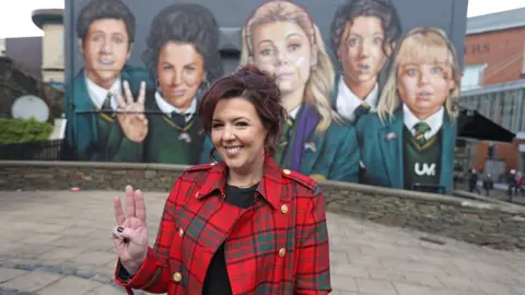 PA/Liam McBurney Writer Lisa McGee in front of a Derry Girls mural in Derry, ahead of the premiere for the third series of Channel 4"s Derry Girls at the Omniplex Cinema in Londonderry