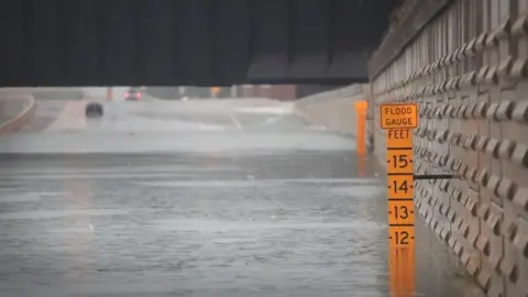 Getty Images A gauge shows the depth of water in an underpass on Interstate 10 which has been inundated with flooding from Hurricane Harvey (27 August 2017)