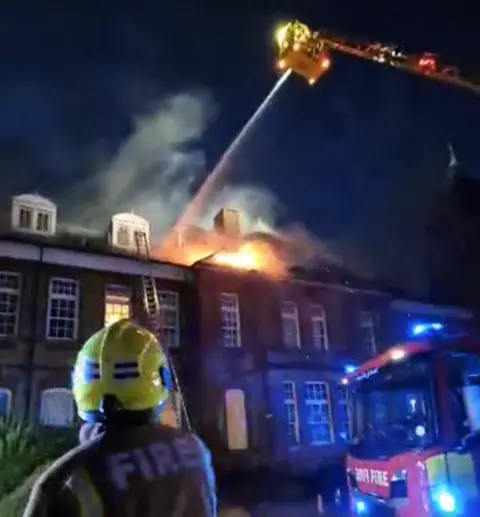 A firefighter watches as his colleagues spray water on the blaze