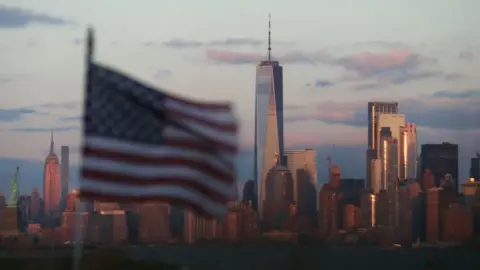 Getty Images An American flag flies in front of The Statue of Liberty, the Empire State Building and One World Trade Center as the sun sets in New York City on December 15, 2019 as seen from Bayonne, New Jersey