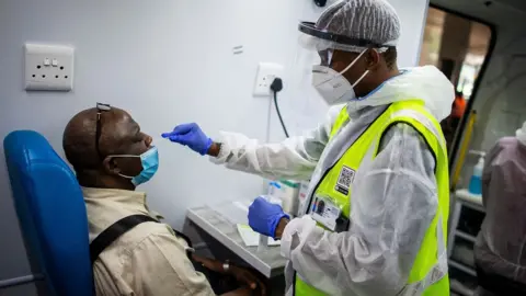 AFP A medical staff member of the South Africa Health Department obtains a nasal swab sample from a passenger in a mobile testing unit at O.R Tambo International Airport in Ekurhuleni on December 30, 3030, where passengers that have COVID-19 symptoms upon arrival are tested. (Photo by Luca Sola / AFP) (Photo by LUCA SOLA/AFP via Getty Images)