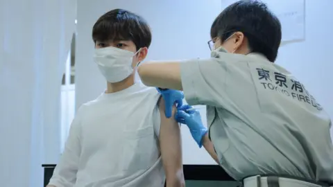 Getty Images A Tokyo fire brigade staff member (right) administers a dose of the Covid-19 coronavirus vaccine at Aoyama University in Tokyo on August 2, 2021