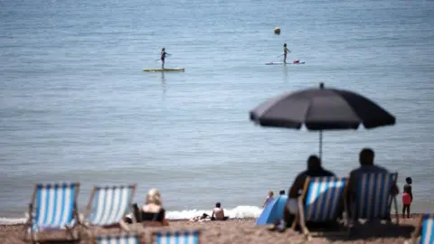 Reuters People paddle board as they enjoy the hot weather at Brighton beach