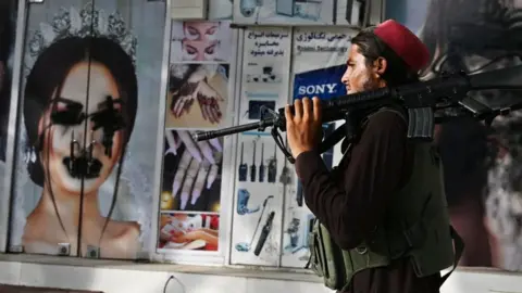 AFP A Taliban fighter walks past a beauty salon with images of women defaced using spray paint in Shar-e-Naw in Kabul on August 18, 2021.