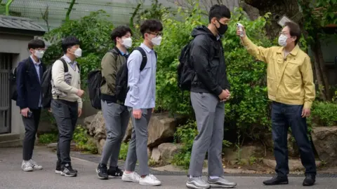 AFP Students returning to school in Seoul in May, wearing face masks and having their temperature checked, after more than two months off due to the pandemic