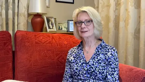 BBC Vivien Prior sitting in her living room on her sofa, smiling at the camera