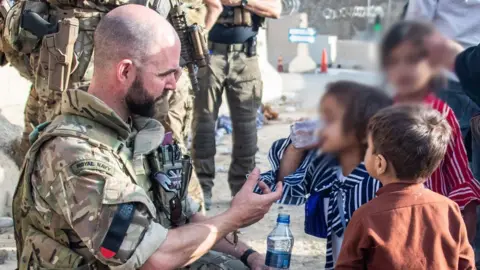 MOD British solider offers water to child at Kabul airport on 23 August 2021