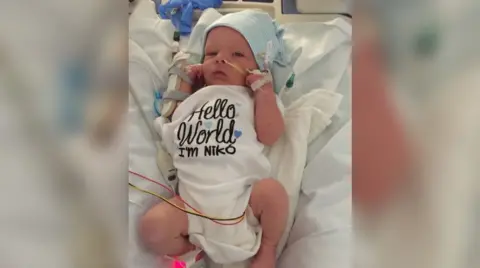 Family photo Niko as a baby wearing a "Hello world, I'm Niko" top