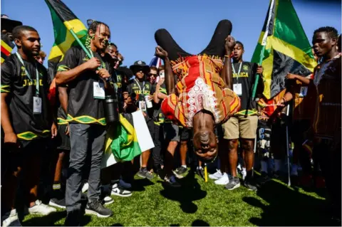 Getty Images Man in African clothes mid-air doing a backflip whilst others look on with Jamaican flags