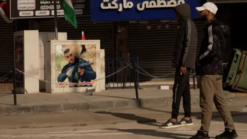 Francesco Tosto/BBC Two youths walk near a picture of a young man with an assault rifle. Photo: 12 December 2023