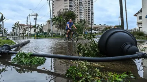 Getty Images A man cycles through water past a downed street lamp in the aftermath of Hurricane Ian in Fort Myers, Florida, on September 29, 2022