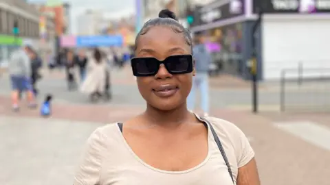 BBC Naz Bajeh stood wearing sunglasses with a street in Southend in the background