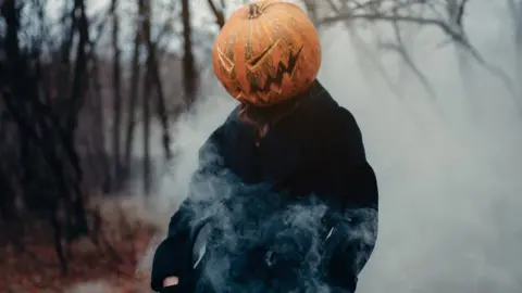 Getty Images A man in a long black coat with a pumpkin instead of a head in a dark, damp and foggy forest.