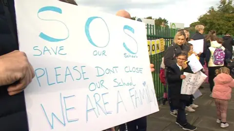 Campaigners outside school holding a save our school banner