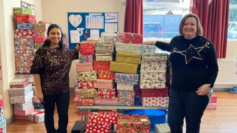 Sewa Day Two volunteers with a pile of Christmas shoeboxes