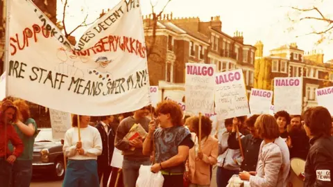 Nursery workers hold white placards calling for better pay and conditions