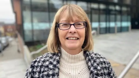 Wendy Randall with long brown hair and glasses standing outside office building