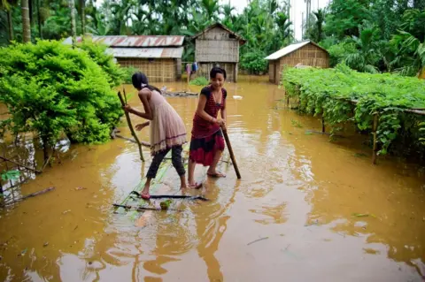 Reuters Girls row a makeshift raft past submerged houses at a flood-affected village in Assam's Karbi Anglong district.