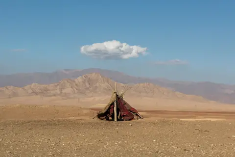 Majid Hojjati Tent in front of mountains, below a small white cloud in the sky