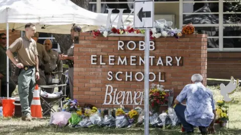 EPA Officers stand near a memorial of flowers at the scene of the mass shooting at the Robb Elementary School in Uvalde, Texas on 25 May