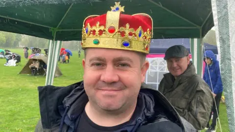 A smiling man wearing a crown under his gazebo