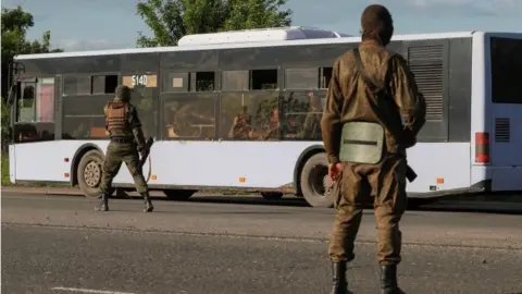 Reuters Russian-backed soldiers guard a bus with Ukrainian soldiers outside Mariupol, south-eastern Ukraine. Photo: May 2022