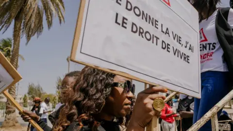 AFP A woman holds a sign during a sit-in to demand justice for Astou Sokhna and call for a more humane and patient-friendly health care system at the Place de la Nation in Dakar on April 23, 2022.