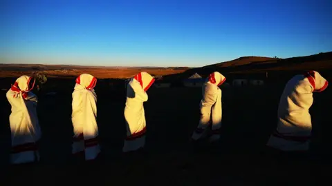 Getty Images Initiates are smeared with white clay on their face and are covered in red and white blankets