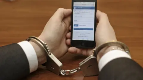 Anton Vaganov/Interpress/ TASS Pictures of hands in handcuffs holding a mobile phone displaying the VKontakte website