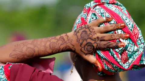 Adekunle Ajayi/Getty Images A woman with henna on her hands and arms attends Eid prayers in Lagos, Nigeria - Wednesday 10 April 2024