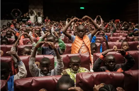 AFP Boys sitting in a theatre doing a ballet move, with their hands above their heads.