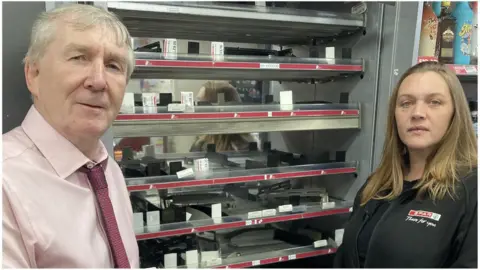 BBC Andrew and Susan Connolly owners of the Spar store in Pewsey standing in front of the empty cigarette cabinet