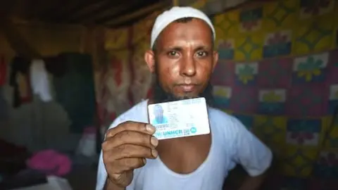 Getty Images A refugee living at the Rohingya refugee camp holds up his UNHCR card at Kalindi Kunj on August 17, 2022 in New Delhi.