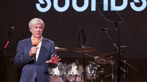 BBC Director General - Tony Hall standing in front of a drum kit at the launch event for BBC Sounds