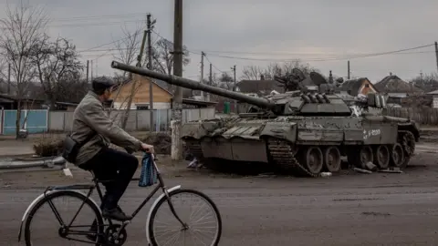 Getty Images A man rides his bike past a destroyed Russian tank on 30 March, 2022 in Trostyanets, Ukraine.