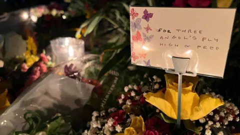 Message left remembering the three children in front of some flowers - "for the angels, fly high and free"