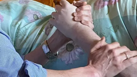 PA Media Embracing hands and arms