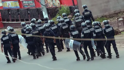 AFP Two dozen police in body armour, helmets, and shields walk down a street away from the camera