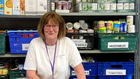 Broke Not Broken stock controller Susan in front of a large shelf full of different types of food