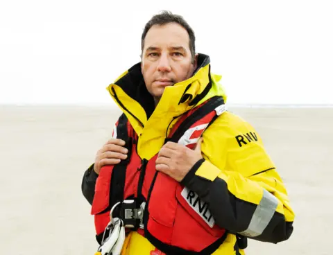 RNLI Daryl James standing in front of the sea in rescue gear