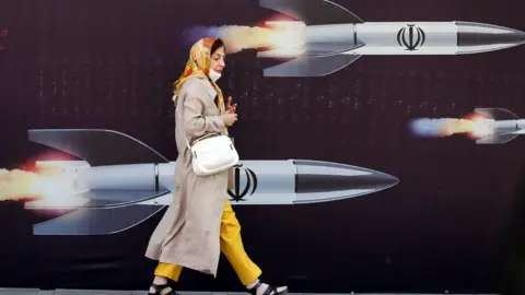 EPA An Iranian woman walks past a huge anti-Israeli banner carrying pictures of missiles, in Tehran, Iran, 19 April 2024.