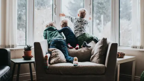 Getty Images Three children looking out of a window.