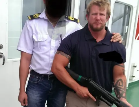 Nick Dunn Nick Dunn holds gun next to ship officer