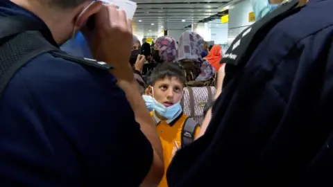 BBC A boy looks on at border force officers