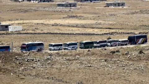 EPA Syrian rebels and families gather to leave at the village of al-Qahtaniah, next to the city of Quneitra, at the Syrian part of the Golan Heights, as seen from the Israeli side of the border, 20 July 2018