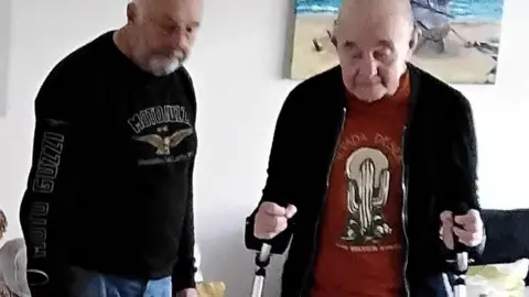 Family photo Harold standing on a walker and friend