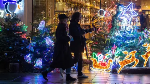 PA Media Shoppers pass a Christmas light display outside a store in Mayfair, in central London